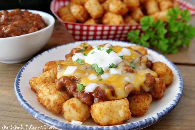 A landscape photo of chili cheese tater tots topped with melted cheese, sour cream, onions, and parsley.