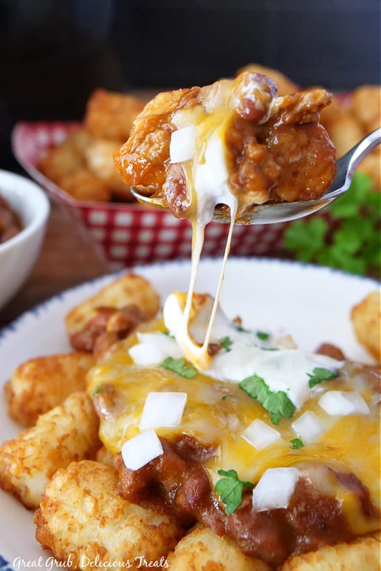 A bite of chili covered tater tots with sour cream on a spoon.