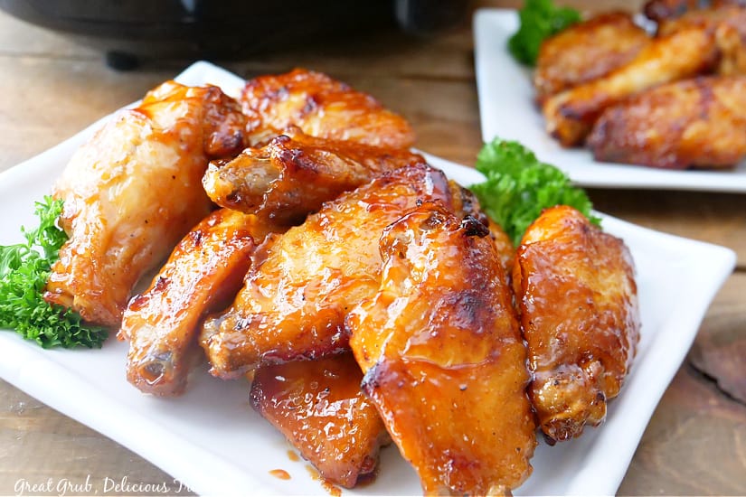 A large pile of honey BBQ chicken wings on a long white plate.