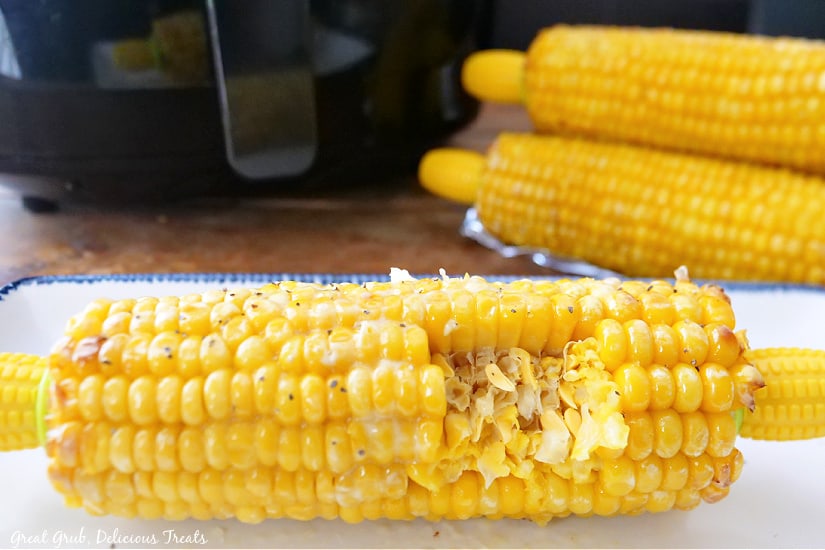 An air fried ear of corn with a bite taken out of it sitting on a white plate.