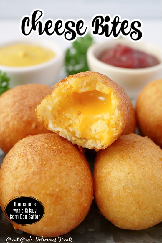 Cheese bites stacked up on a silver tray with a bite taken out of one, showing melted cheddar cheese in the middle.