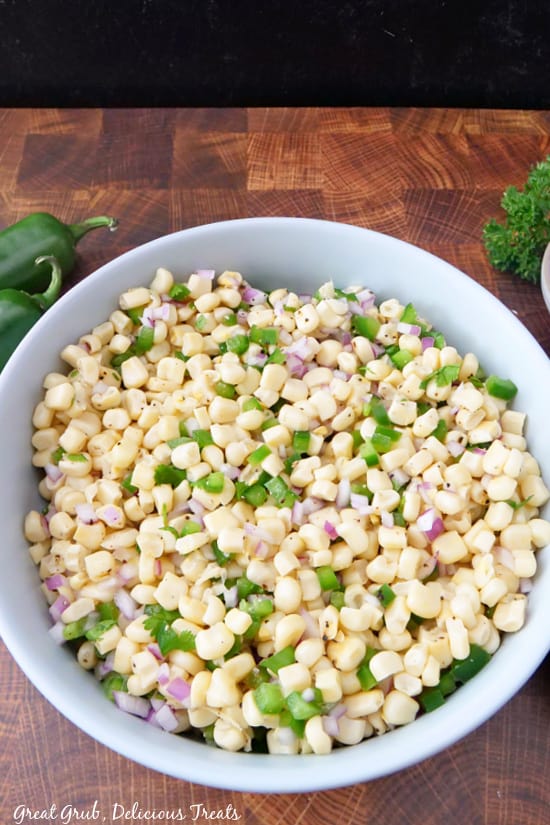 A very large bowl filled with corn salsa, showing corn, red onions, jalapenos, and seasoning.