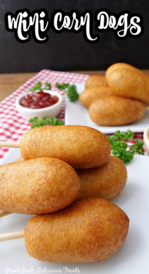 Two plates with corn dogs on them, sitting on a red and white plaid placemat.