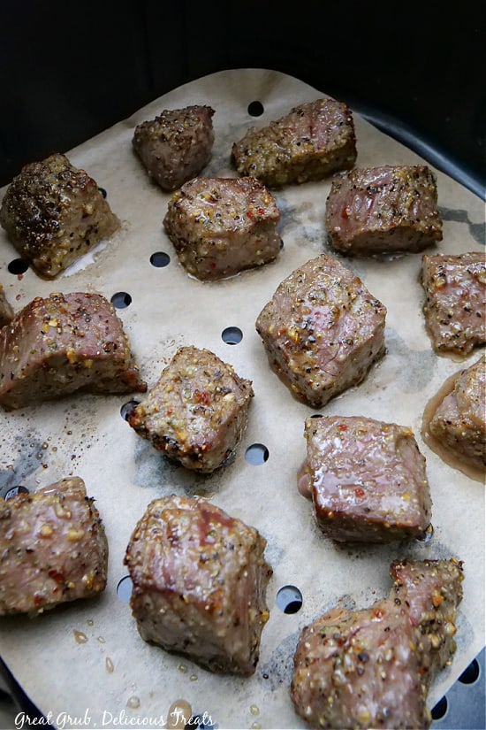 Steak bites placed in an air fryer basket lined with parchment paper.