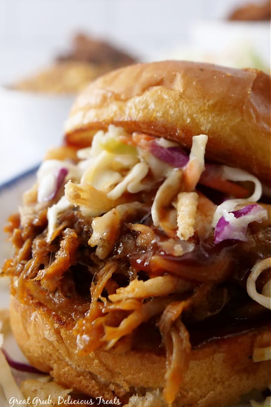 A close up photo of a slider with pulled pork, onion strings, coleslaw, ad BBQ sauce.