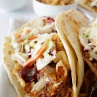 A pulled pork taco on a white plate topped with crispy onion strings and shredded cabbage.