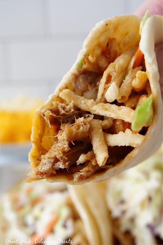 A taco filled with pulled pork, onion strings, and shredded cabbage.