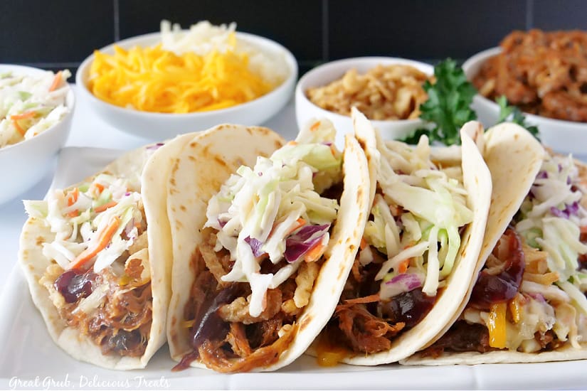A long plate lined with pulled pork tacos.