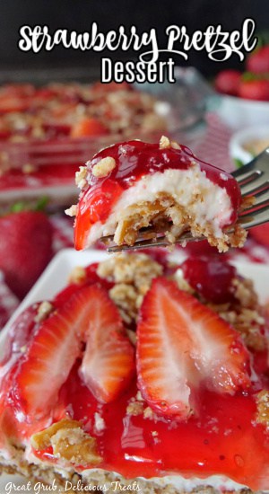 A square of dessert with sliced strawberries on top and a bite of dessert being held up over it.