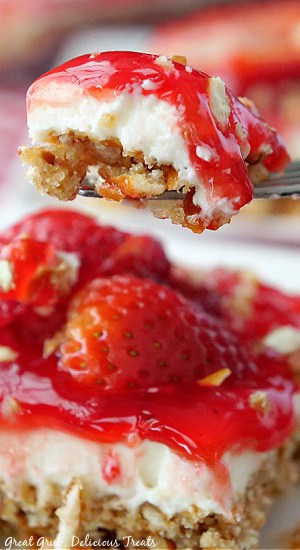 A bite of dessert being held up on a fork sitting above a square of strawberry dessert.
