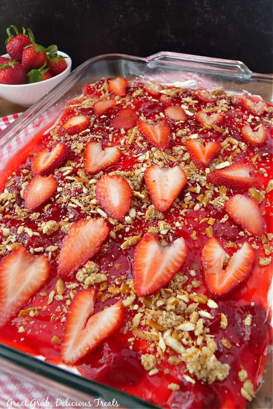 A baking dish with dessert in it, with sliced strawberries on top and crushed pretzels. 