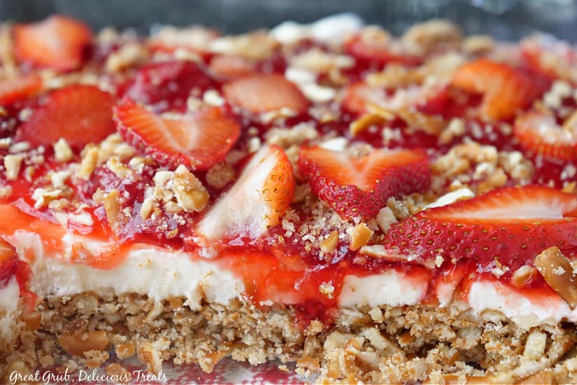 A landscape photo of dessert showing the layers of pretzel crust, cream cheese, strawberry pie filling, and sliced strawberries on top.