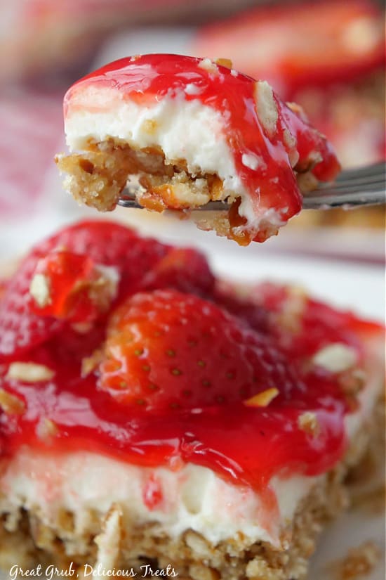 A bite of strawberry dessert being held up over a square of dessert. 