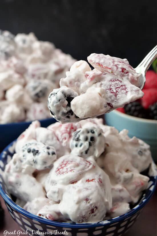 A close up photo of a spoonful of fruit salad with berries and mini marshmallows. 