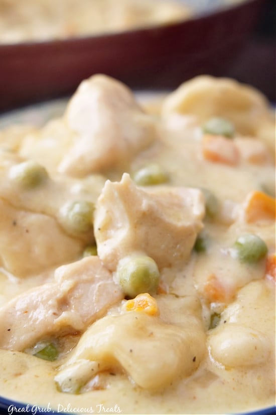 A close up photo of chicken and dumplings, showing the dumplings, chicken, and veggies in it.