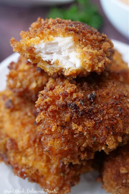 A close up of a stack of chicken bites on a white plate with a bite taken out of one of them.