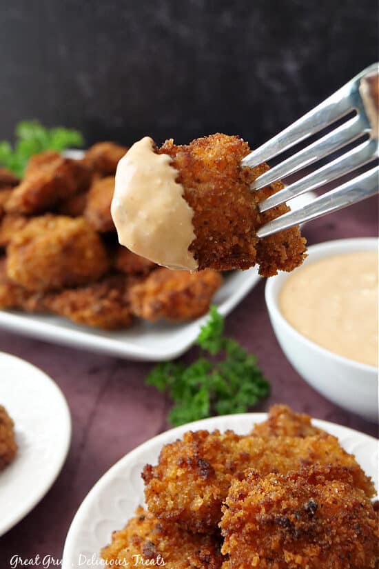 A fried chicken bites of a fork that was dipped in comeback sauce.