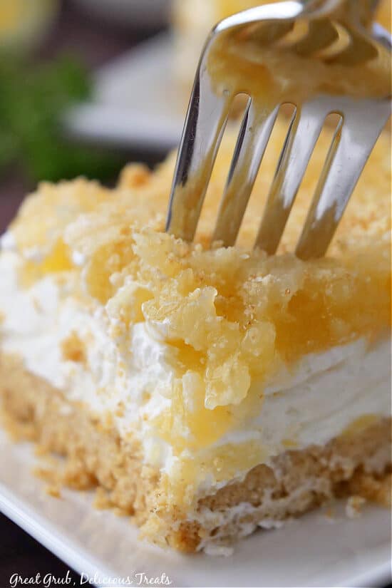 A close up of a slice of pineapple dessert on a white plate with a fork pressed into the dessert.