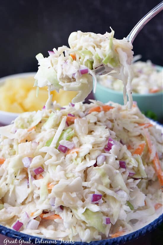 A close up of a spoonful of coleslaw being held above a bowl filled with coleslaw.
