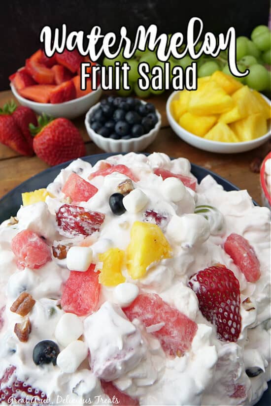 A close-up picture of Watermelon Fruit Salad in a bowl with fruit in the background and the title at the top.