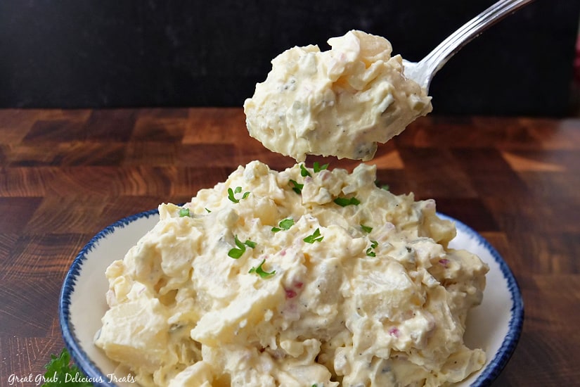 A bite of potato salad being held over a bowl of potato salad.