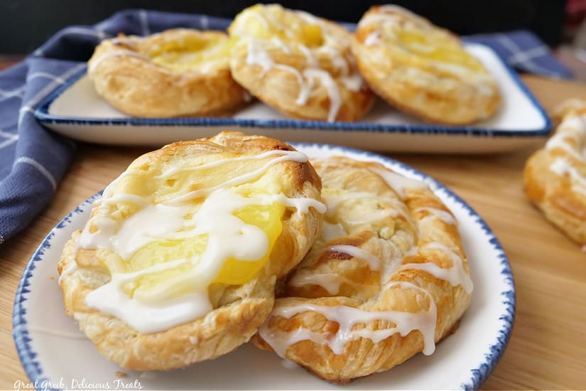 Two lemon Danishes on a white plate with blue trim and three more in the background.