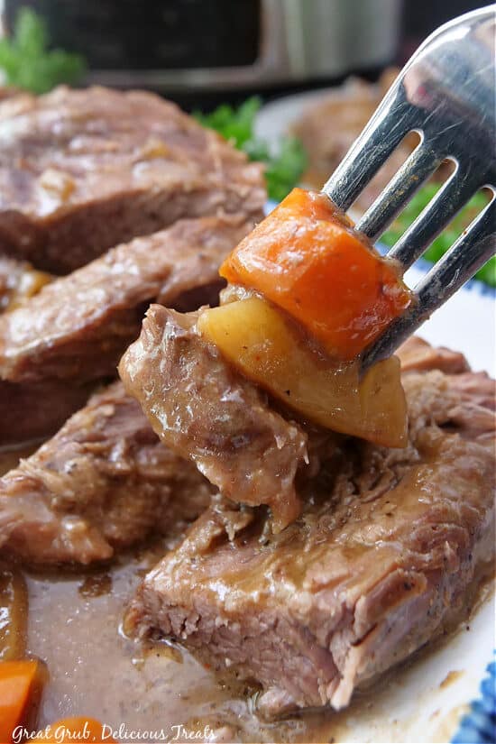 A close up of a bite of roast, potato and carrot on a fork.