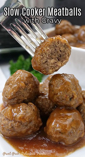 Meatballs on a white plate with a meatball with a bite taken out of it on a fork.