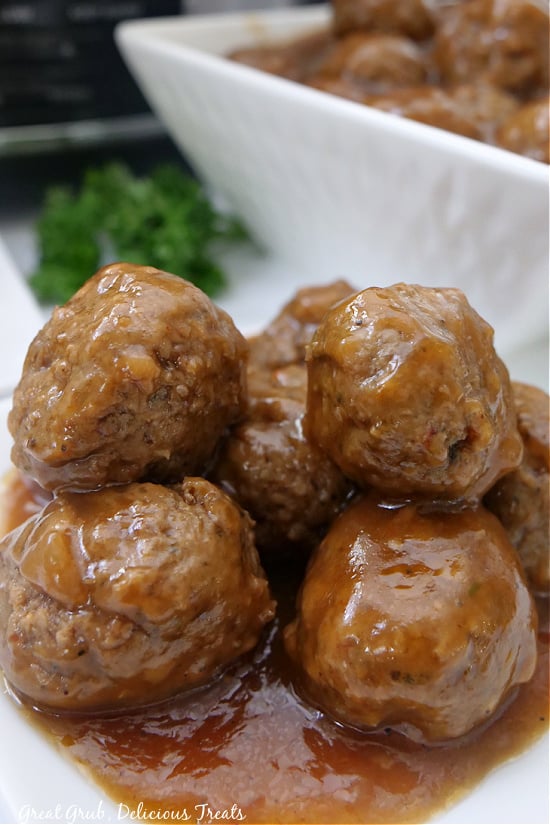 A white bowl filled with meatballs in the background and meatballs stacked on a white plate.