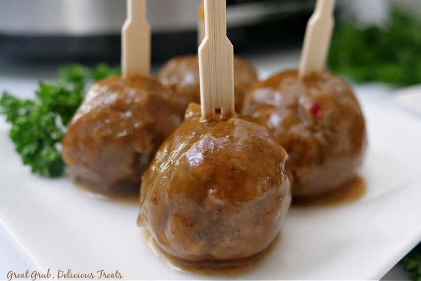 Four meatballs on a white plate with toothpicks in them.