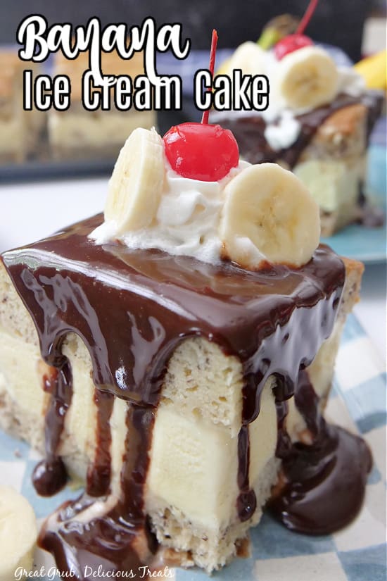 A slice of banana cake with hot fudge on top, a dollop of whipped cream, two slices of bananas, and a maraschino cherry. 