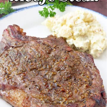 A perfectly cooked ribeye steak on a white plate with blue trim, served with a side of country style potato salad.