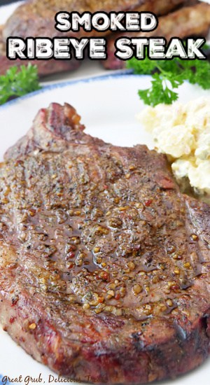 A ribeye steak sitting on a white plate with a serving of potato salad next to it.