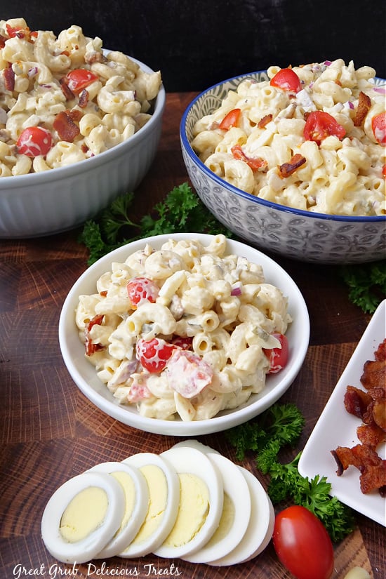 Three bowls filled with bacon pasta salad on a brown wooden surface.