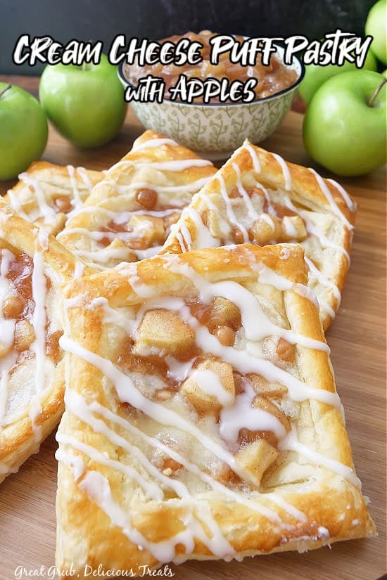 Four cream cheese pastries on a wooden board, with green apples, and apple filling in the background.