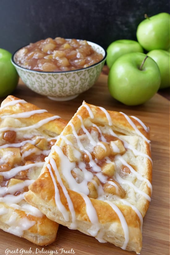 A wooden board with two apple pastries on it.