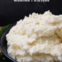 A serving of mashed potatoes in a black bowl, topped with black pepper.