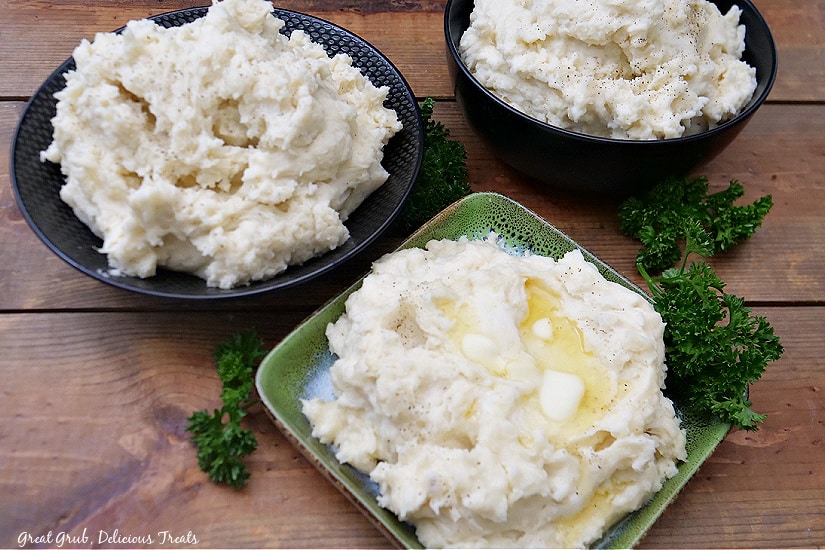 A landscape photo of three bowls of mashed potatoes on a wood board.