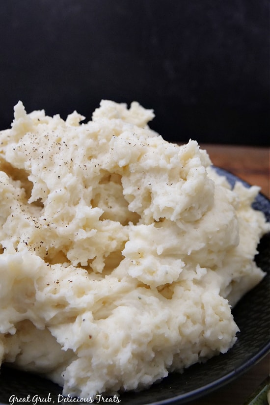A large black bowl filled with mashed potatoes, topped with cracked black pepper.