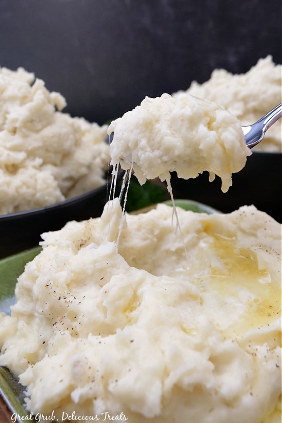 A bite of mashed potatoes on a spoon, holding up over a bowl of mashed potatoes.