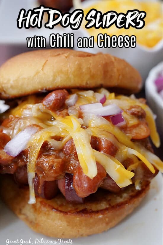 A close up of a slider bun with a hot dog, chili, cheese and onions on it.