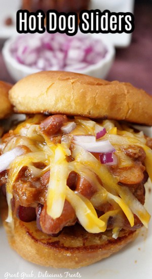A close up of a hot dog slider on a white plate with shredded cheese, diced onions, chili and hot dog.