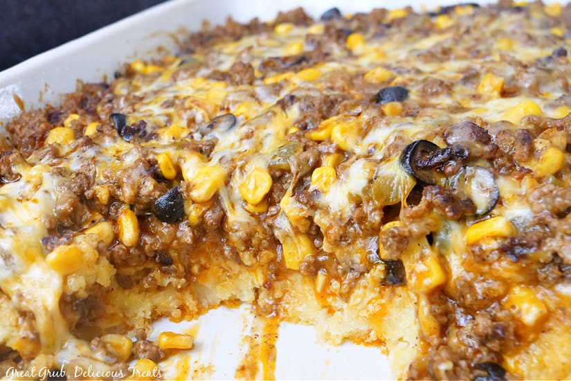 A casserole dish with Mexican Tamale Pie in it showing the different layers, cornbread, meat mixture, cheese.