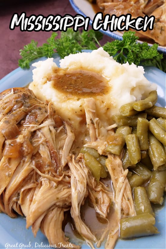 A serving of Mississippi chicken on a blue plate with mashed potatoes, green beans, and gravy.