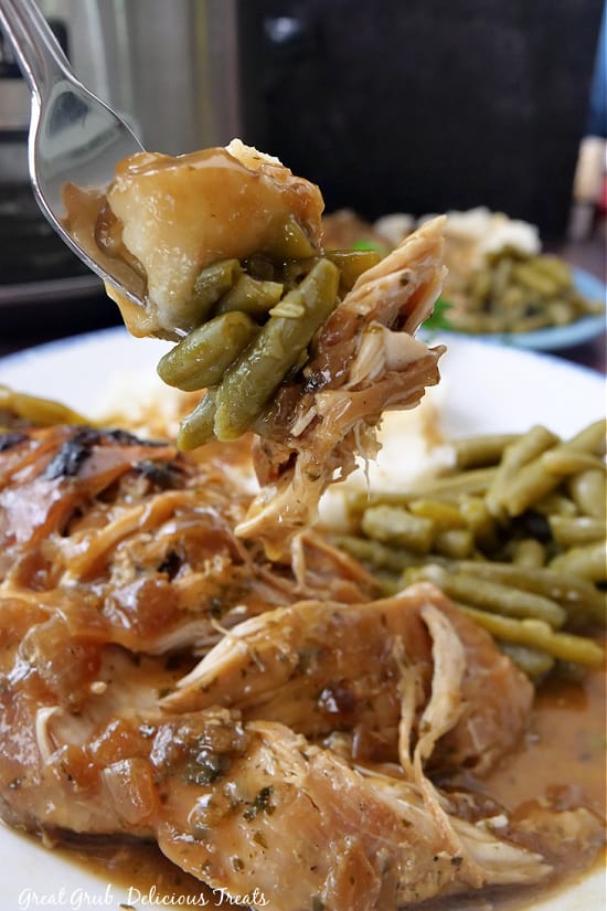 A bite of Mississippi chicken on a fork with green beans and mashed potatoes.