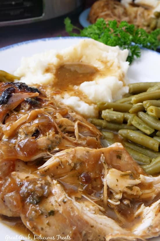 A large serving of tender Mississippi chicken with mashed potatoes and green beans with gravy on top.