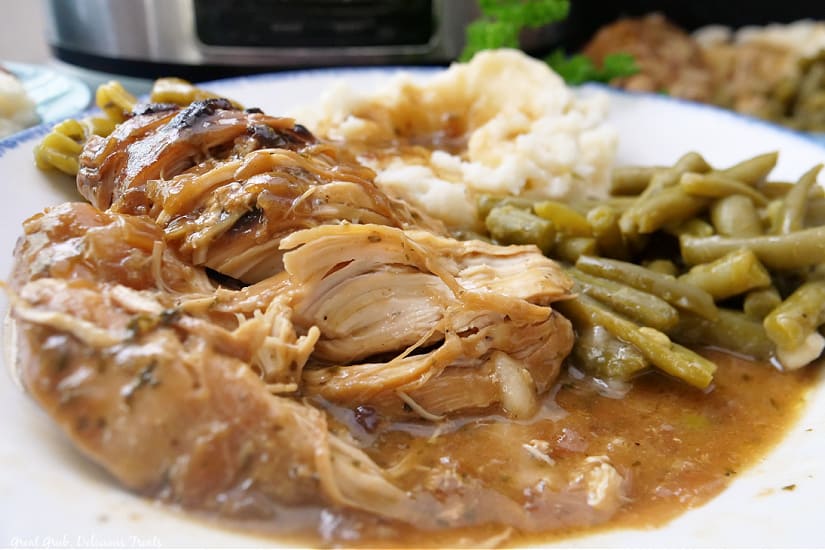 A landscape photo of a chicken, potatoes, and green beans on a white plate, all covered in gravy.