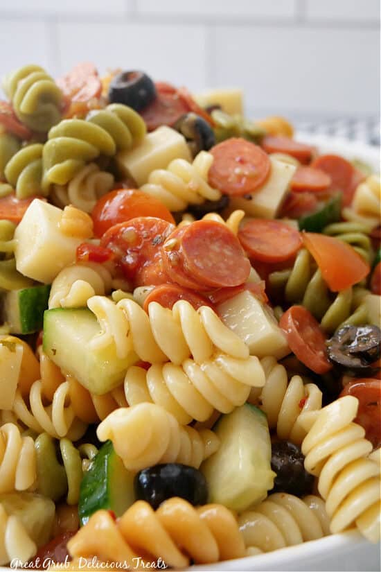 A super close up of pasta salad showing the rotini pasta, mini pepperonis, black olives, cucumbers, chunks of cheese.