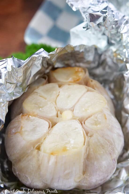 A close up of a head of garlic with aluminum foil wrapped around it after being air fried.