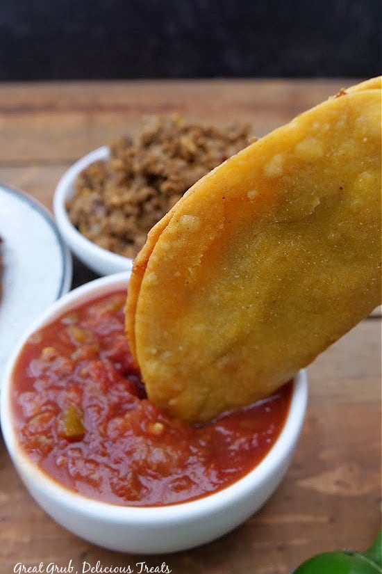 A taco being dipped into a white bowl full of salsa.